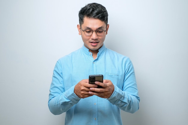 Souriant jeune homme asiatique beau utilisant un smartphone pour entrer en contact avec sa famille et ses amis isolés