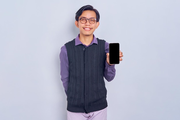 Souriant jeune homme asiatique en chemise décontractée et gilet montrant un téléphone portable à écran blanc isolé sur fond blanc Concept de style de vie des gens