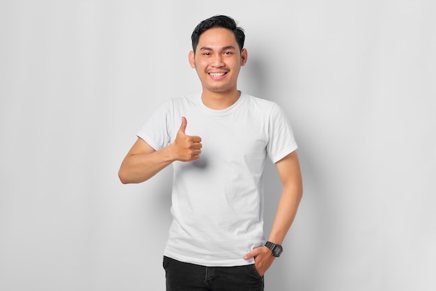 Souriant jeune homme asiatique montrant le geste du pouce en l'air approuvant l'expression en regardant la caméra isolée sur fond blanc