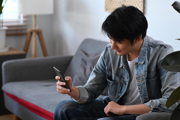 Souriant Jeune Homme Asiatique Se Détendre Sur Un Canapé à La Maison Et Utiliser Un Téléphone Portable Concept De Personnes Et De Technologie