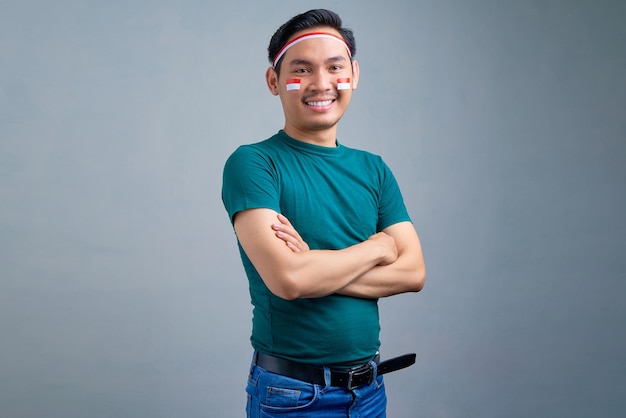 Souriant jeune homme asiatique en t-shirt décontracté debout avec les bras croisés regardant la caméra isolée sur fond gris concept de célébration de la fête de l'indépendance de l'indonésie