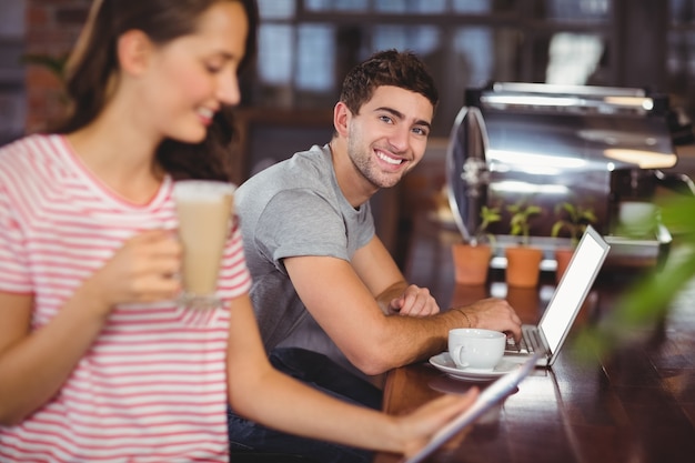 Souriant jeune homme assis au bar et en utilisant un ordinateur portable