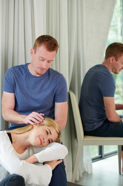 Souriant jeune homme attentionné donnant un massage relaxant de la tête à sa petite amie reposant la tête sur ses genoux