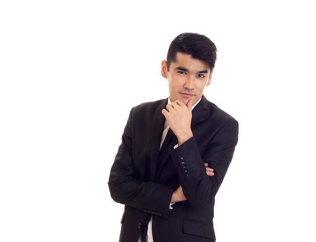 Souriant jeune homme aux cheveux noirs en chemise blanche et costume noir avec cravate noire sur fond blanc