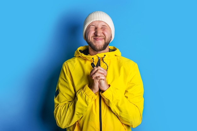 Souriant jeune homme fermant les yeux fermés avec les bras croisés en jaune sur fond bleu