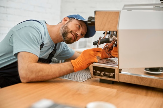 Souriant jeune homme fixant la machine à café au café