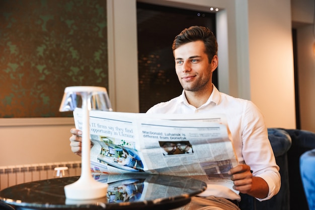 Souriant jeune homme habillé formel lisant le journal