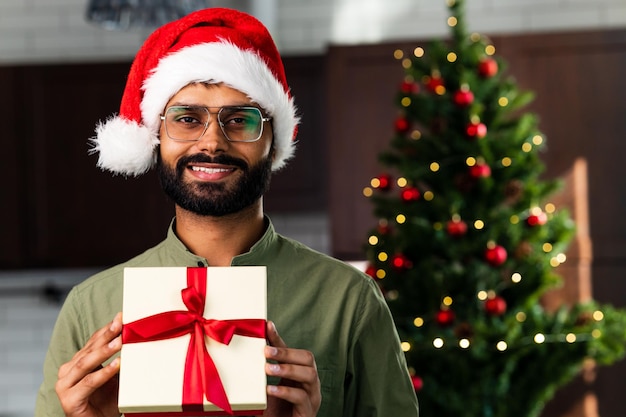 Souriant jeune homme hispanique latin tenant un cadeau de Noël à la maison