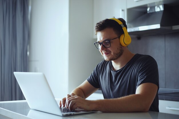 Souriant jeune homme indépendant utilisant un ordinateur portable étudiant en ligne travaillant à domicile