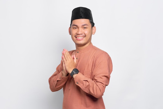 Souriant jeune homme musulman asiatique gesticulant Eid Mubarak salutation isolé sur fond blanc