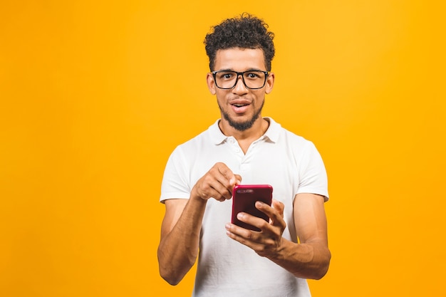 Souriant jeune homme noir dans des verres tenant le téléphone isolé sur jaune