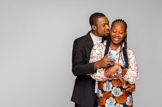 Photo souriant jeune homme noir embrassant une femme par derrière tout en regardant le smartphone. couple afro-américain partageant les médias sociaux sur téléphone portable, femme heureuse