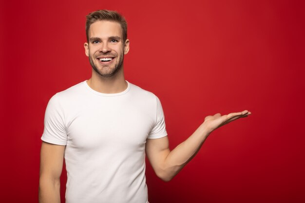 souriant jeune homme pointant avec la main de côté isolé sur rouge