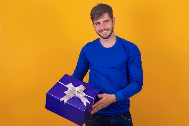 Souriant jeune homme tenant une boîte-cadeau sur fond jaunejeune garçon tenant une boîte-cadeau sur fond jaune