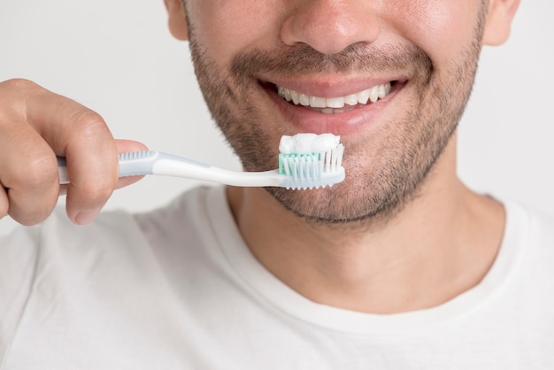 Photo souriant jeune homme tenant une brosse à dents avec de la pâte