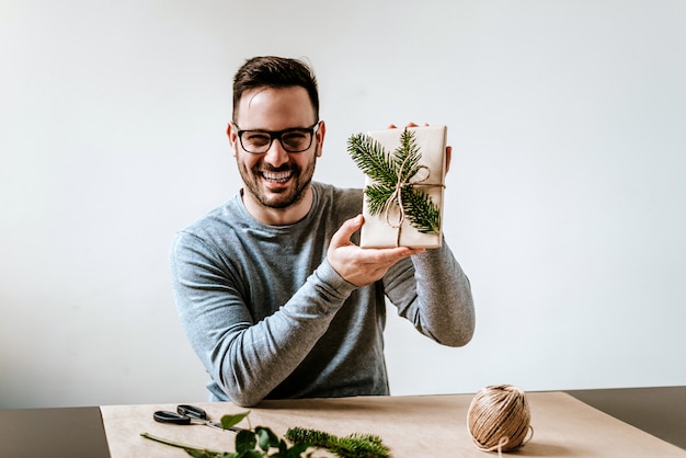 Souriant jeune homme tenant un cadeau qu&#39;il a emballé.