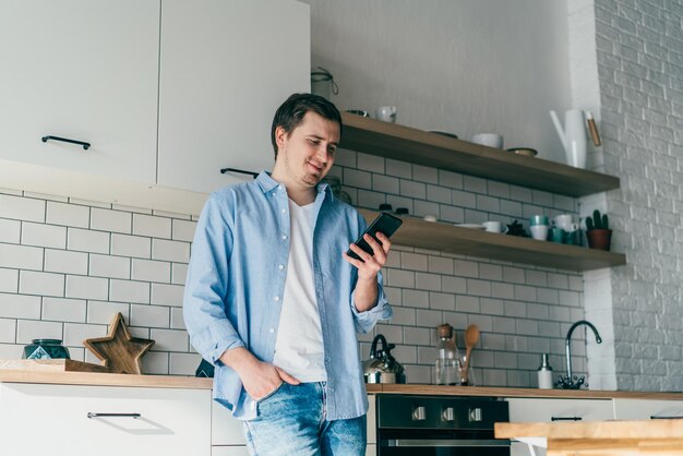 Photo souriant jeune homme utilisant un smartphone dans la cuisine