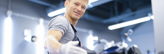 Souriant jeune mécanicien automobile se tient en gros plan de l'atelier