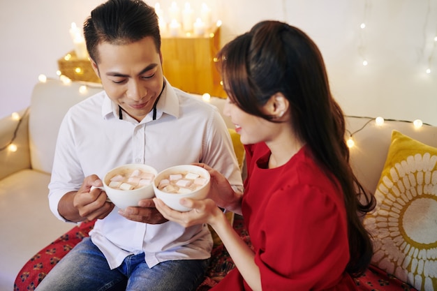 Souriant jeune petit ami et petite amie asiatique buvant du chocolat chaud avec des guimauves