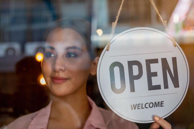 Souriant jeune propriétaire d'entreprise asiatique, employé de vente au détail, femme de café, fille tournant, plaçant le panneau d'affichage à ouvrir pour accueillir le client, rouvrir le magasin après avoir fermé la quarantaine de verrouillage dans le concept covid.Label.