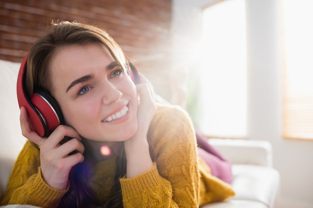 Souriant jolie femme écoutant de la musique allongé sur le canapé dans le salon