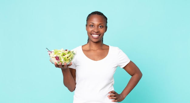 souriant joyeusement avec une main sur la hanche et confiant et tenant une salade