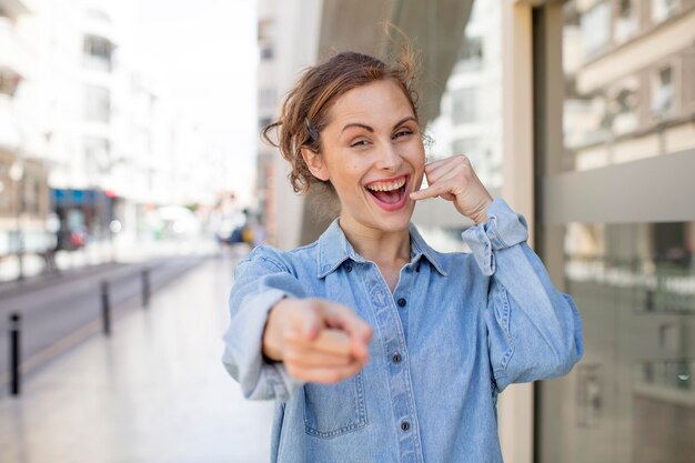 Souriant joyeusement et pointant vers la caméra tout en passant un appel, vous faites plus tard un geste en parlant au téléphone