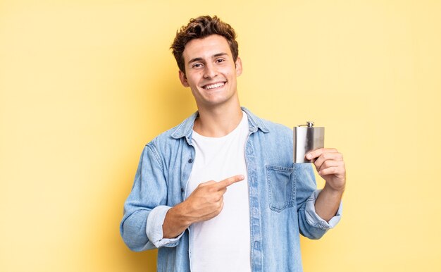 souriant joyeusement, se sentant heureux et pointant vers le côté et vers le haut, montrant l'objet dans l'espace de copie. concept de flacon d'alcool