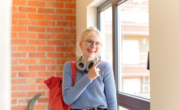 souriant joyeusement, se sentant heureux et pointant vers le côté et vers le haut, montrant l'objet dans l'espace de copie