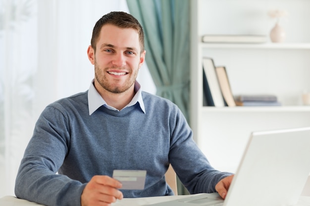 Souriant mâle avec carte de crédit sur son ordinateur portable