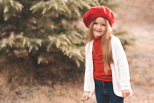 Souriant mignon enfant fille 4-5 ans porter un béret rouge et une veste tricotée en plein air dans le parc