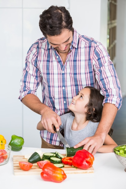 Souriant père enseignant fille à couper des légumes