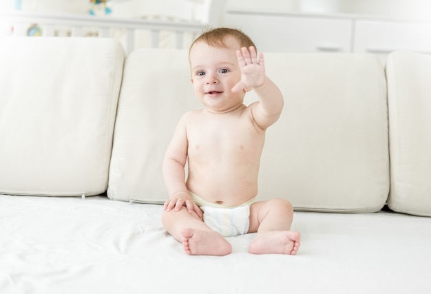 Souriant petit garçon en couches assis sur le lit