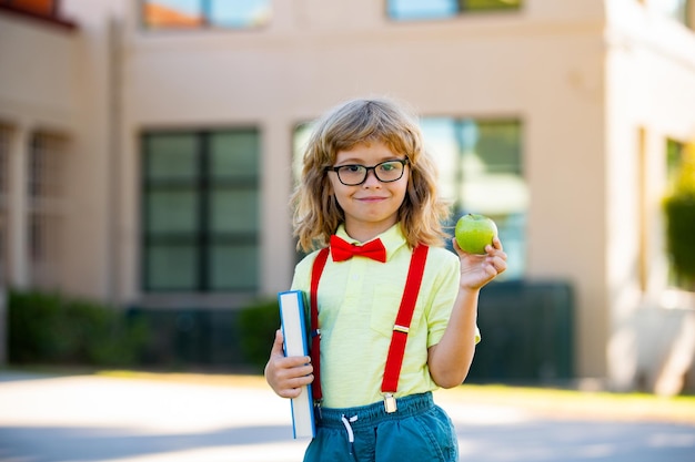 Photo souriant petit garçon étudiant portant un sac à dos scolaire et tenant un cahier d'exercices. portrait d'élève heureux à l'extérieur de l'école primaire. gros plan du visage d'un écolier hispanique souriant regardant la caméra.