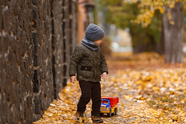 souriant petit garçon marchant et jouant avec la petite voiture à l'extérieur en automne. concept de l'enfance heureuse. portrait d'enfant drôle