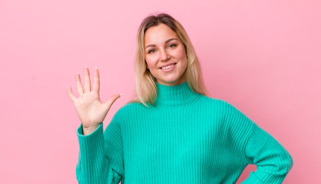 souriant et à la recherche amicale montrant le numéro cinq ou cinquième avec le compte à rebours vers l'avant de la main