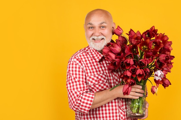 Souriant retraité mature avec barbe tenir des fleurs de tulipes printanières sur fond jaune