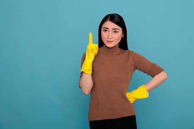 Souriant Satisfait Ravi Femme De Ménage Asiatique Portant Des Gants Jaunes Et Pointant Le Doigt Vers Le Haut Pour Copier L'espace, Concept De Maison De Nettoyage, Femme De Ménage Optimiste Et Positive De Glade