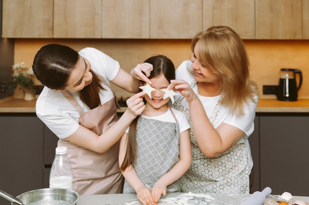 Souriant trois générations de femmes s'amusent à faire des gâteaux sucrés à la maison ensemble petite fille avec jeune mère et grand-mère cuisinent dans la cuisine