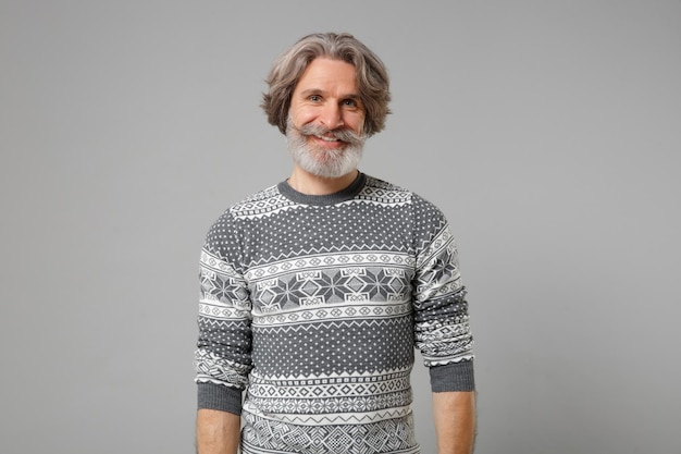 Souriant vieil homme barbu moustache aux cheveux gris en chandail tricoté posant isolé sur fond gris, portrait en studio. Concept de mode de vie des émotions sincères des gens. Maquette de l'espace de copie. Regarder la caméra.