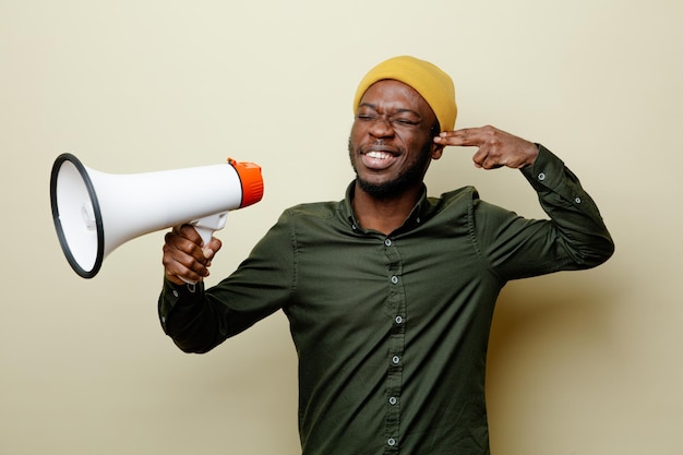 Souriant avec les yeux fermés jeune homme afro-américain en chapeau portant une chemise verte tenant un haut-parleur isolé sur fond blanc