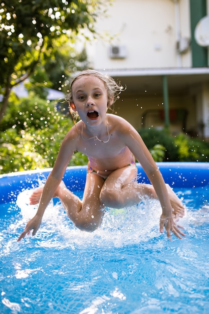 Souriante adorable fille de sept ans jouant et s'amusant dans la piscine gonflable.