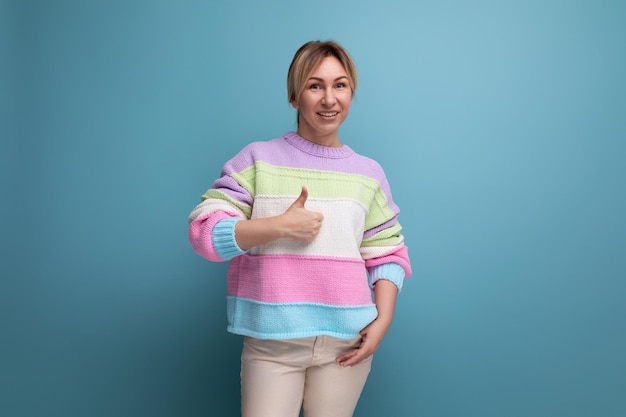 Souriante agréable jeune femme blonde dans un pull rayé montre comme avec sa main sur un bleu