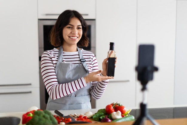 Souriante belle femme brune enregistrant un vlog alimentaire cuisinant à la maison