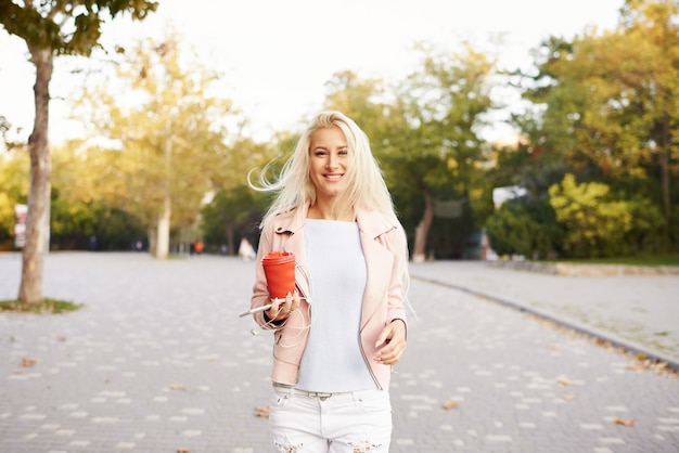 Souriante belle femme écoutant de la musique relaxante dans les écouteurs avec son téléphone portable ou sa tablette dans le parc. l'étudiant écoute une conférence en ligne et se prépare aux examens.