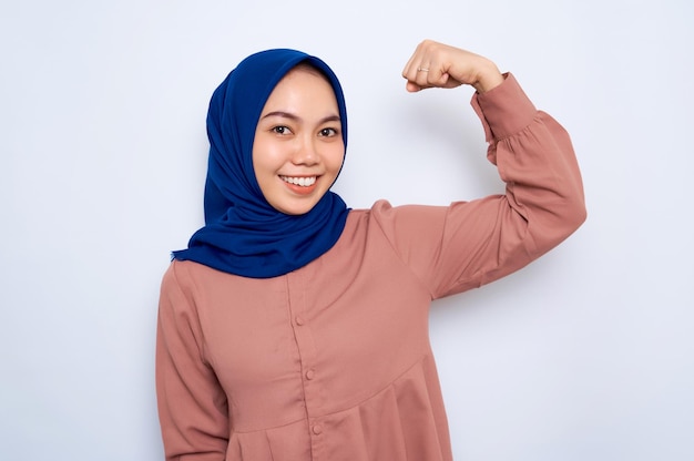 Souriante belle femme musulmane asiatique en chemise rose lève les bras et montre les biceps a démontré sa réussite après une formation dans une salle de sport isolée sur fond blanc Concept de style de vie religieux des gens