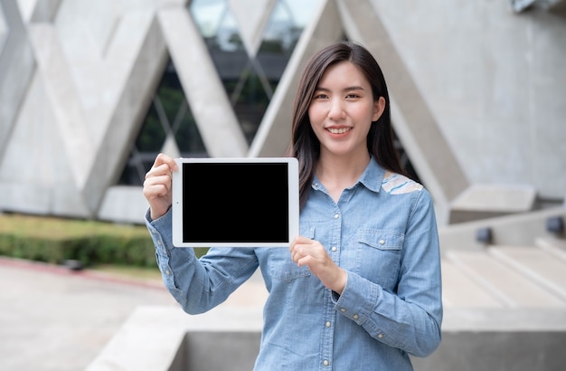 Souriante belle jeune femme d'affaires brune montrant un moniteur de tablet pc vierge sans nom