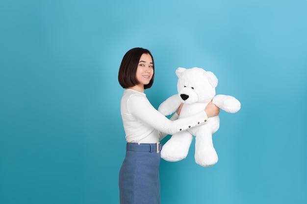 Souriante belle jeune femme asiatique se tient sur le côté et tient un grand ours en peluche blanc