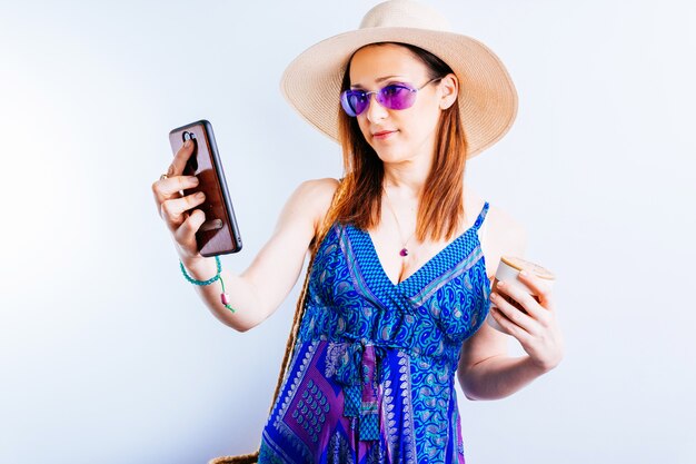 Souriante belle jeune femme habillée pour textos plage d'été sur le smartphone en vacances sur fond blanc