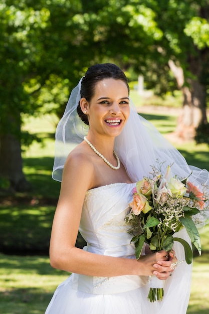 Souriante belle mariée avec bouquet debout dans le parc